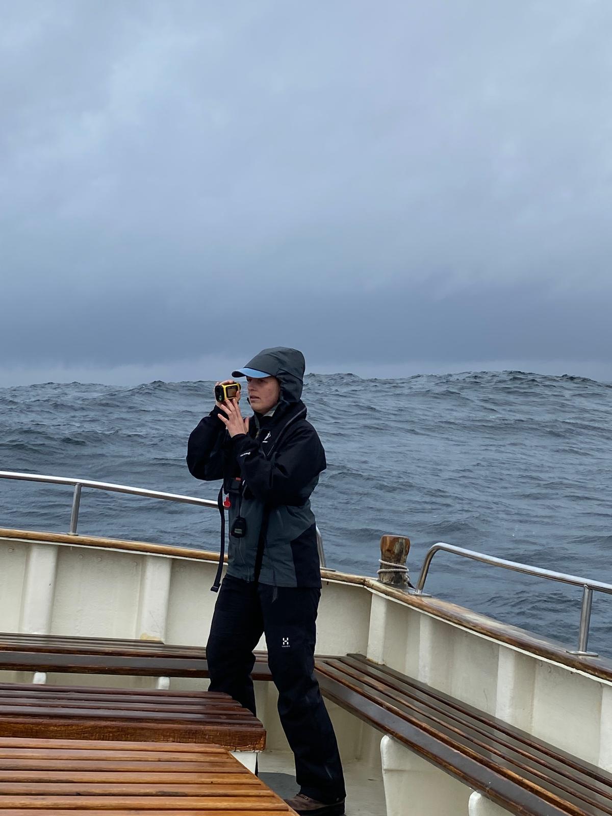 Photographer of a fieldworker using a laser rangefinder on a small boat in rough sea conditions. Image courtesy of Orea Anderson