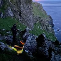 Photograph of a fieldworker on a cliffside St Kilda at sunset (image courtesy of Brennig Hughes)